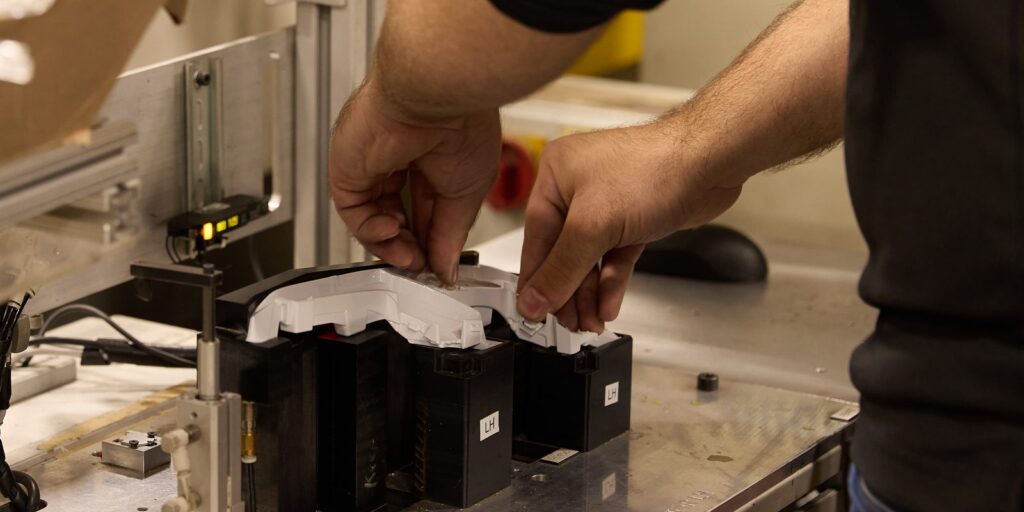 Operator's hands seating a white molded housing into an LH assembly fixture