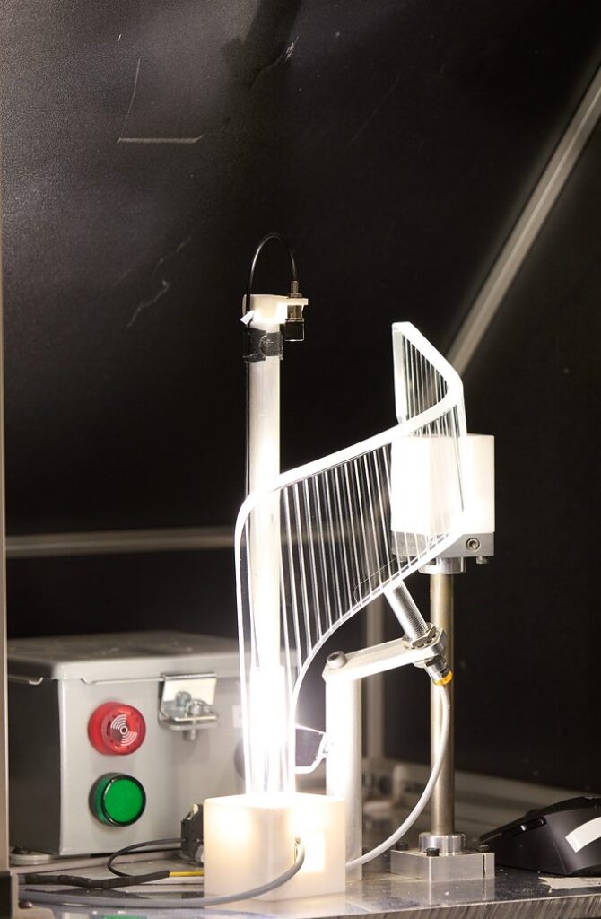 Clear molded automotive light guide glowing on a light-test stand during inspection