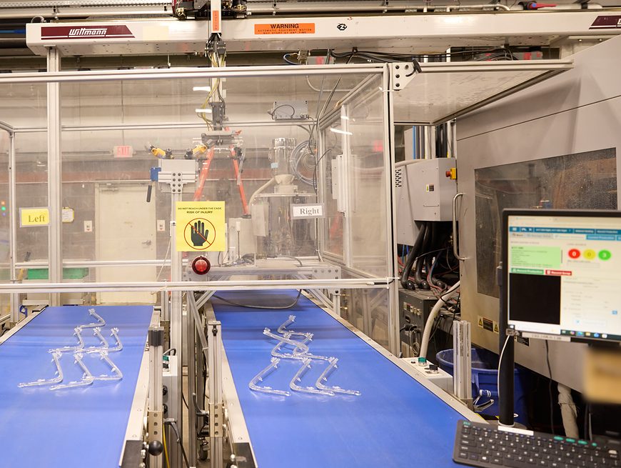 Production monitoring screen beside a robot cell with clear molded parts on two conveyors