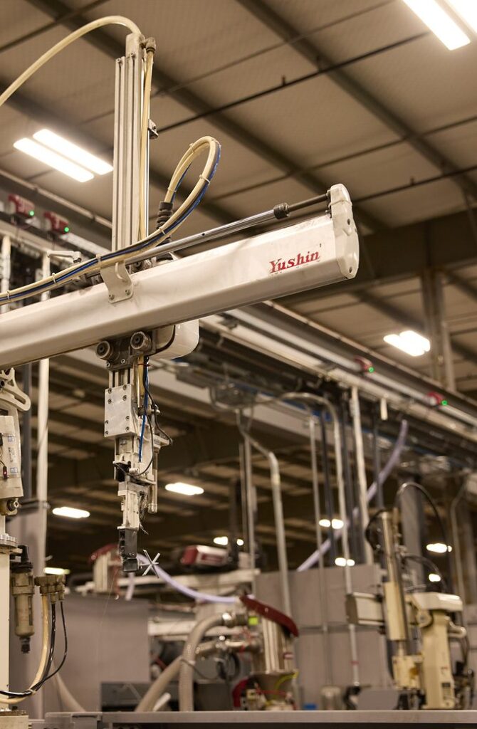 Take-out robot arm mounted on an injection molding press, seen against the plant ceiling
